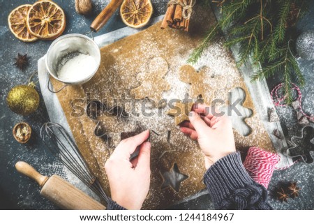 Girl cooking christmas homemade gingerbread star cookies, gingerbread men, flat lay, top view, with accessories ingredients for baking. Dark blue concrete background, copy space, hands in picture