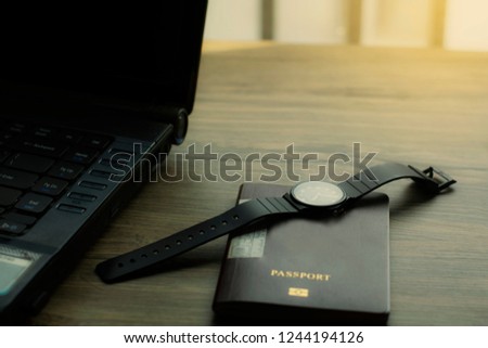 black laptop with brown passport and watch on top back solf light