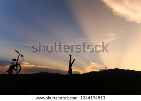 Silhouette of happy child playing upside down outdoors in summer park walking on hands at sunset