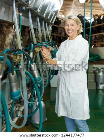 Portrait of mature woman in white coat working with milking line on farm