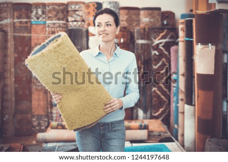 Cheerful woman customer choosing  colored carpet in carpet store