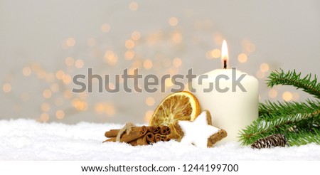 
Christmas background - candle with pine branches and spices in the snow with blurred lights in the background
