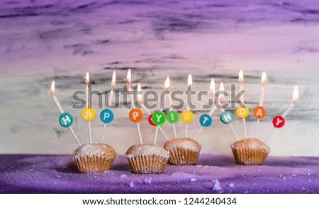 sweet cupcakes with a colorful Happy Birthday sign and candles on purple pastel background