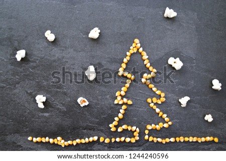 Popcorn corn shapes a Christmas tree on a dark background with popcorn as snowflakes - concept with corn in the shape of a Christmas tree and popcorn as snow in the background