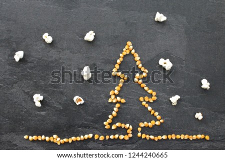 Popcorn corn shapes a Christmas tree on a dark background with popcorn as snowflakes - concept with corn in the shape of a Christmas tree and popcorn as snow in the background