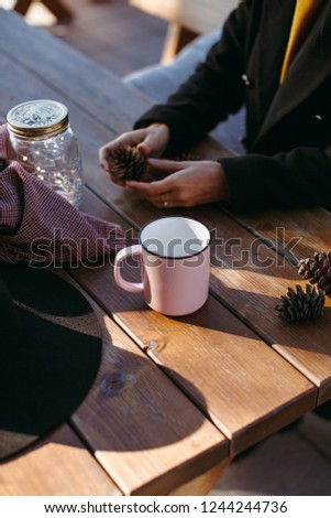 A pink mug, hate, scarf, lights, fir cones on the wooden table