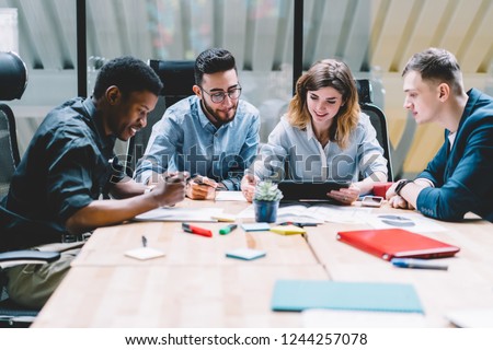 Multicultural group of professional designers collaborating on task using modern touch pad device during brainstorming meeting in office interior. Four employees discussing work with productivity Royalty-Free Stock Photo #1244257078
