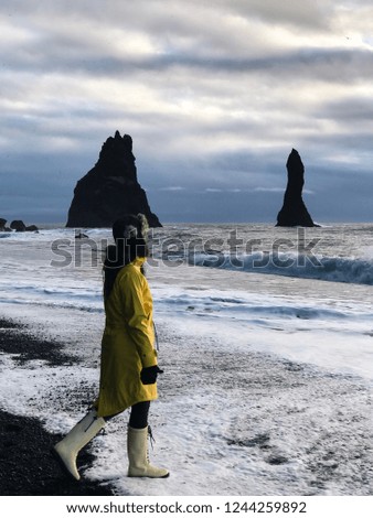 Young woman in a yellow raincoat standing on the black sand volcanic beach. Wonderful landscape view Iceland. Reynisdrangar. National park Iceland.