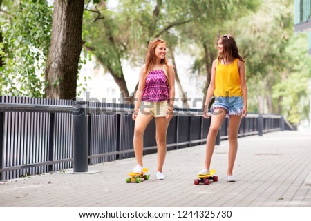 friendship, leisure and people concept - happy teenage girls or friends with short skateboards on city street in summer