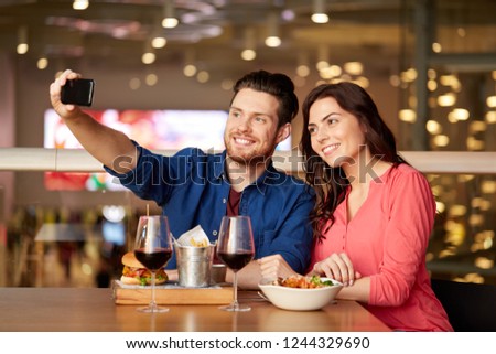 leisure, technology and people concept - happy couple having lunch and taking selfie by smartphone at restaurant