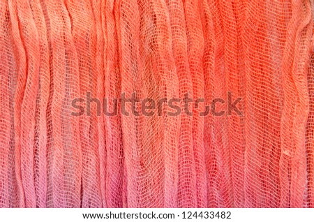 Crinkly, loosely woven  material with an orange to pink color fade.