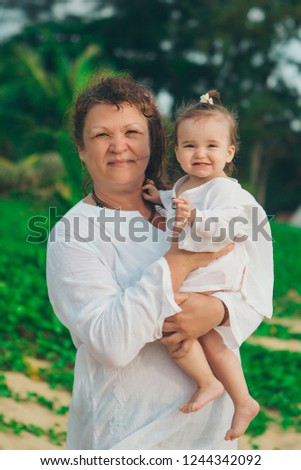 baby in the arms of the mother. Woman holding a child on beach and tropical vegetation background