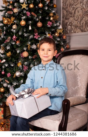 portrait of a boy sitting in an armchair near a christmas tree with a gift box in his hands