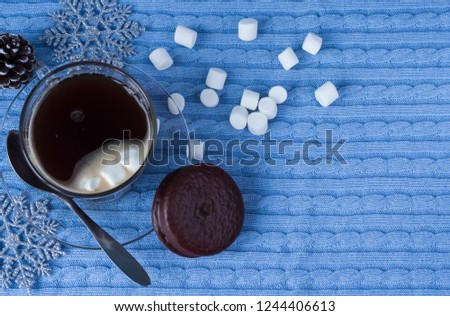 a Cup of Christmas hot coffee with marshmallows and cookies on a blue textile background with copy space