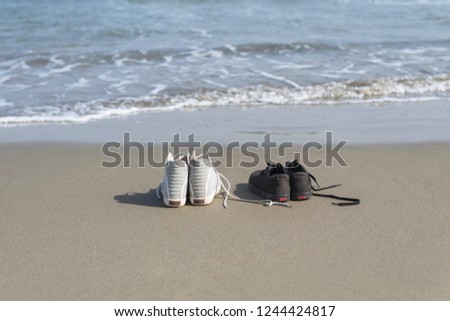 Black and white sneakers on the sand on the sea background. Summer and travel concept 