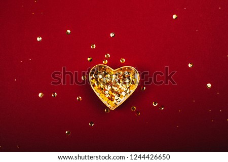 Heart shaped box with golden sequins on red background. Flat lay style. Festive concept.