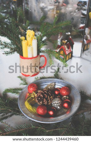 Сandles in a cup and plate with balls and pine cones. Christmas decor for the holiday table