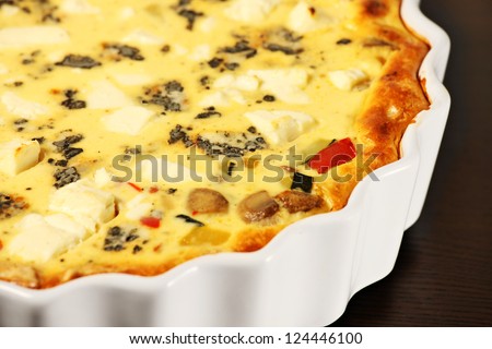 A picture of freshly baked vegetable tart in a white tin over wooden surface