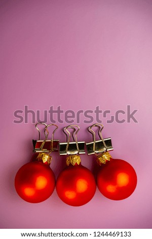 Three toy red balls with office clips lie on a purple background. Christmas composition, winter season.
