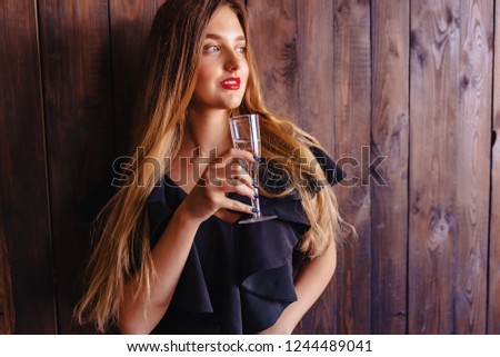 young attractive girl with a glass of champagne or wine on the dark background of the wall