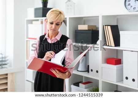 A young girl stands in the office with a red folder in her hands.