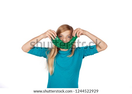 Cute girl holding a green slime toy and making smile with it in front of her face. Studio isolated on white background