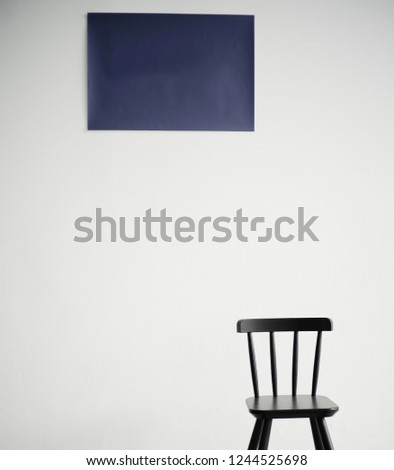 A black wooden chair is standing in front of a white wall with navy picture.