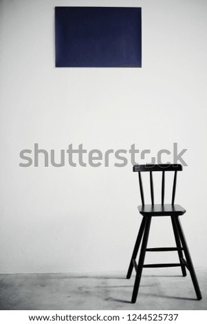 A black wooden bar chair is standing in front of a white wall with navy picture.