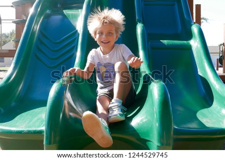 Smiling boy going down a slide with his hair raised due to static electricity Royalty-Free Stock Photo #1244529745