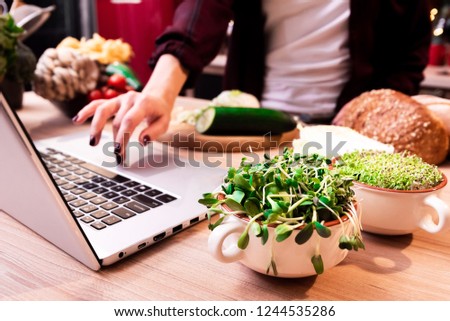 women in the kitchen searching for recipes on his laptop with food ingredients and fresh vegetables. seedlings. wide angle. close up