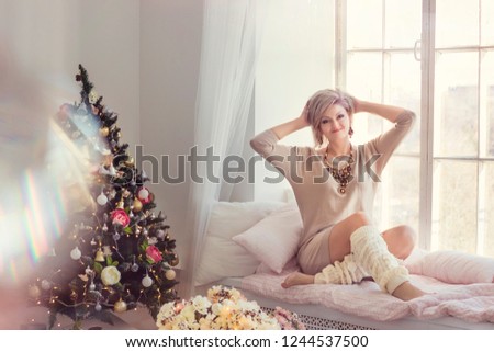 Blonde girl on the windowsill in the new year's morning and Christmas tree on background close-up shallow depth of field