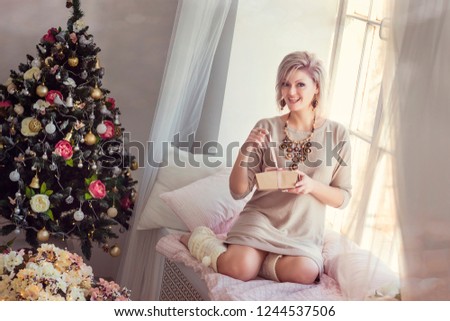Blonde girl on the windowsill in the new year's morning and Christmas tree on background close-up shallow depth of field