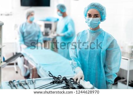 Waist up portrait of female medical worker in protective mask preparing for surgery. Surgeon and his assistant on blurred background Royalty-Free Stock Photo #1244628970