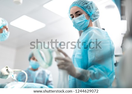 Portrait of young surgical nurse in sterile glove holding respiratory equipment for patient. Focus on lady face in protective mask