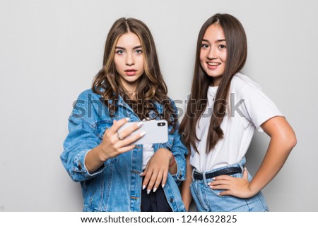 Two girlfriend with phone in hands looking at camera isolated on gray
