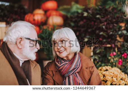 Portrait of smiling lady looking at husband with love and admiration. Flowers and pumpkins on blurred background