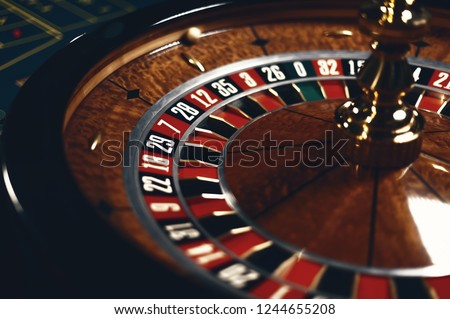Roulette table in casino, with many games and slots, roulette wheel in the foreground. Golden and luxury light, casino interior. Gambling is the wagering of money or playing games of chance for money Royalty-Free Stock Photo #1244655208