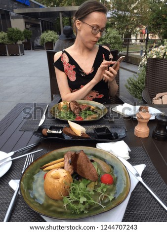 Young woman is making picture of food with mobile phone. Second course: pork meat with apples. Dinner in latvian restaurant.