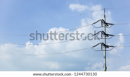 Closeup of concrete electric pylon and group of birds on it and blue sky white clouds.