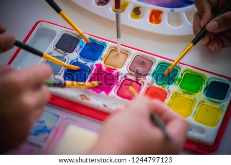 Hands is catching the paintbrush to the colorful watercolor table set on the table, education and art object.