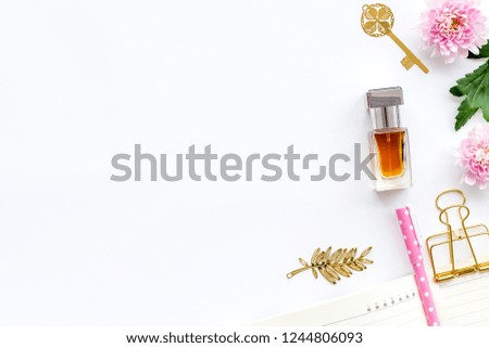 Perfume on feminine desk. Women's accessories. Perfume near notebook for dairy among flowers on white background top view space for text