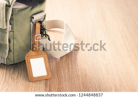 a blank leather luggage tag hanging at the canvas shoulder bag on space of wood floor