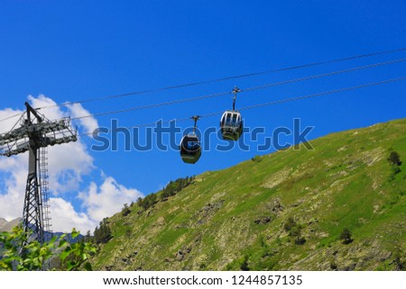Сableway moving up over a Caucasus mountains against clear blue sky and white cloud