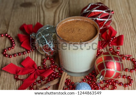 egg nog in glass with cinnamon on top, wooden background. Ornaments and Christmas decor all around. close up, holiday drink, nobody