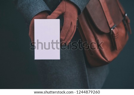 Mock up with white box from a smartphone. The girl in a coat and brown gloves holds a gift in his hands