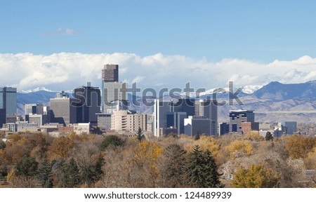 Skyscrapers in Denver, Colorado, with backdrop of the snowy Rocky Mountains and storm clouds.