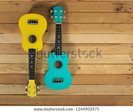 Photo shot of guitar, ukulele on wooden background. Music card, picture, poster. Wooden backdrop, blue and yellow guitars