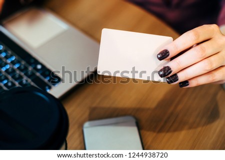 Caucasian female hands holding a bank card over the table with a laptop, phone and coffee.