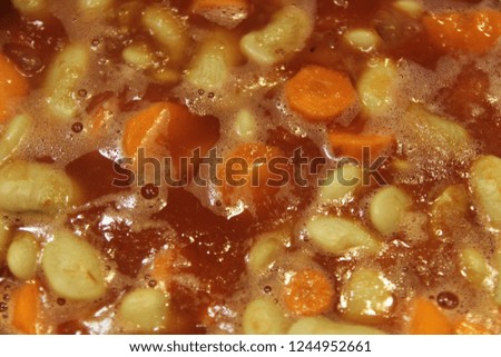 Close up boiling traditional greek bean soup (fasolada) in a pot with carrots and red tomato sauce