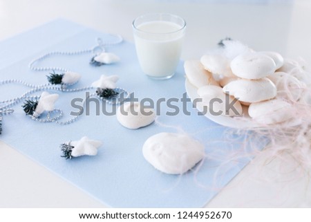Homemade meringue cookies and glass of milk decorated with feather grass and christmas garland on light blue felt background